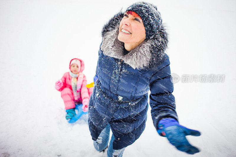 微笑的母亲拉着女儿的雪橇在她身后