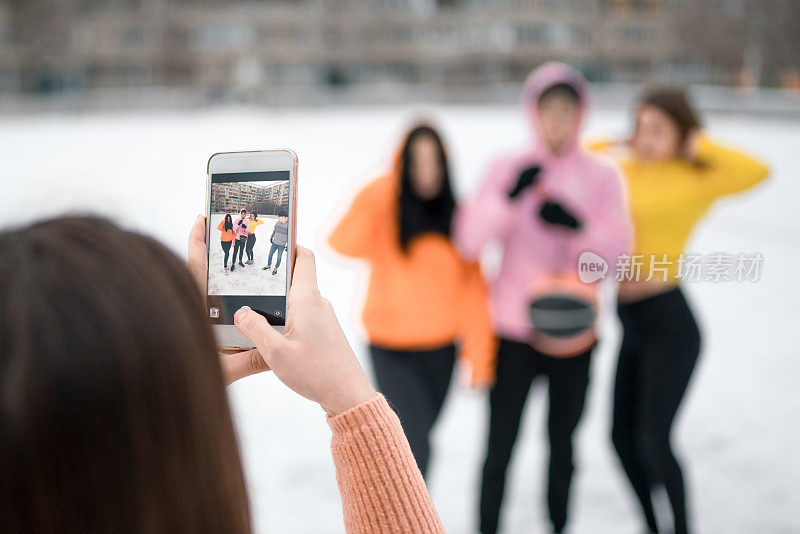 冬天，女孩在户外用手机给青少年朋友拍照