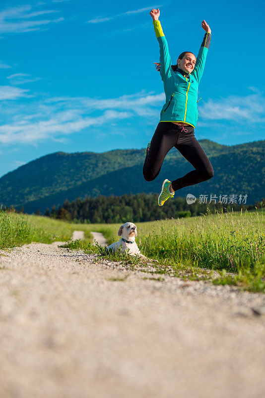 快乐的年轻女子在空中跳跃时，跑在乡村道路上