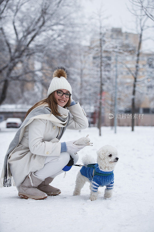 小女孩在白雪覆盖的公园里和狗玩耍