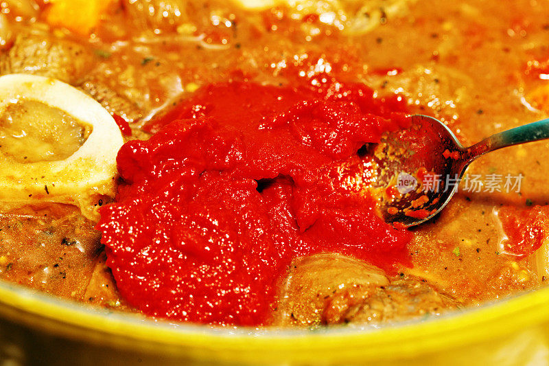 用勺子搅拌番茄酱到牛肉砂锅中