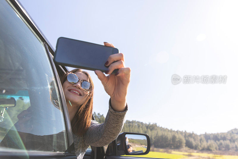 一名女子在公路上开车，一边自拍一边用智能手机发送信息