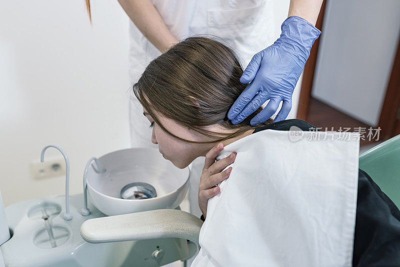 牙医正在为正在用水漱口的年轻病人进行牙科干预