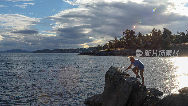 成熟的男人在日出时爬上海滩的岩石
