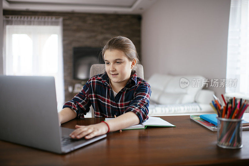 年轻女孩坐在客厅的书桌前用笔记本电脑做作业