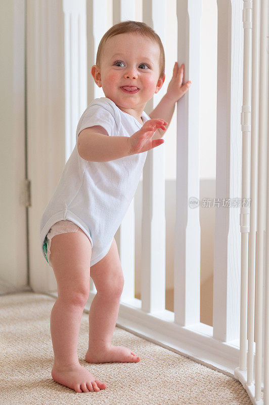 9个月大的男婴站在栏杆旁微笑着看向别处