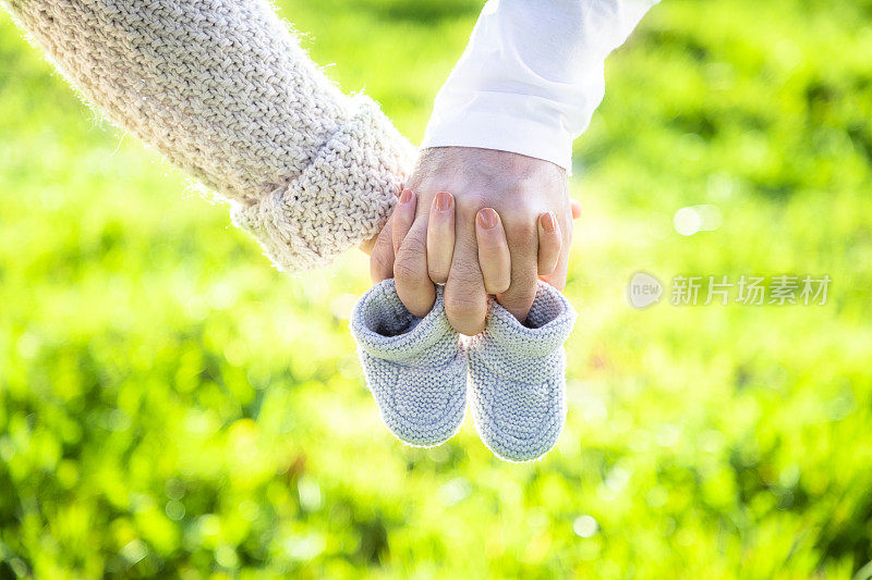 未来的父母手牵着手，穿着一双婴儿鞋