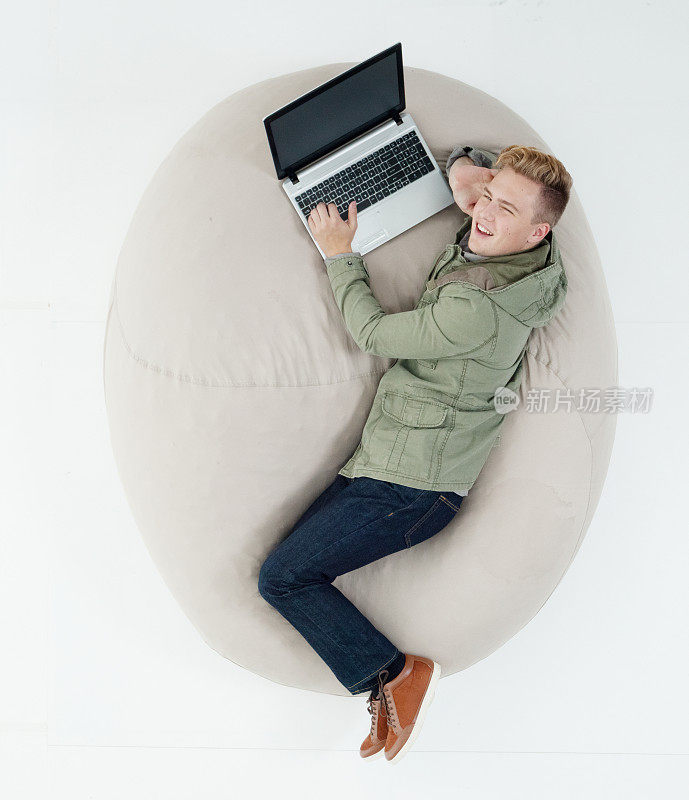 白人男性躺在白色背景下，穿着运动夹克，使用电脑