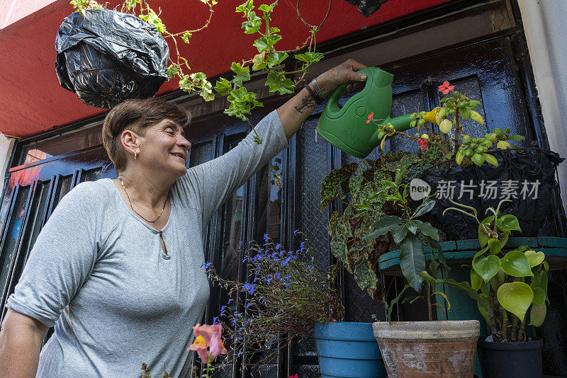 一位年长的拉丁妇女在自家阳台上浇花