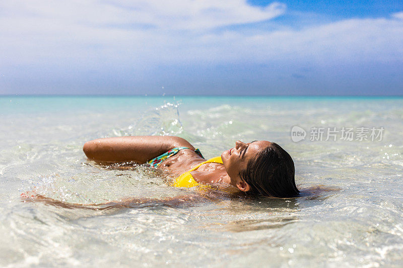 快乐的女人享受日光浴在海滩浅水。