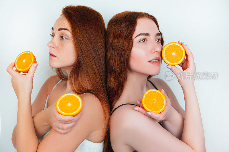 两个红发年轻女性都拿着一半的橙色在他们的手站在他们的背后转向孤立的白色背景，美丽的肖像概念