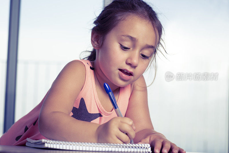 一个小女孩在笔记本上写字。写作阶段。儿童写作在家里的发展。