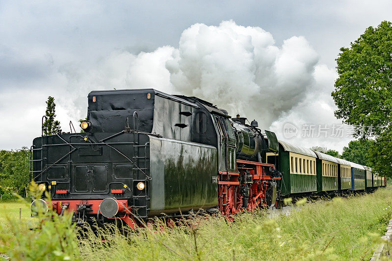 老式蒸汽火车拖着火车车厢在乡村景色中行驶