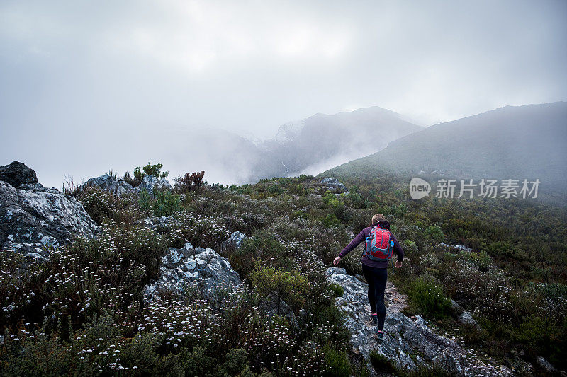 一个健康的女人在一个寒冷的冬天的早晨独自在山里徒步旅行。