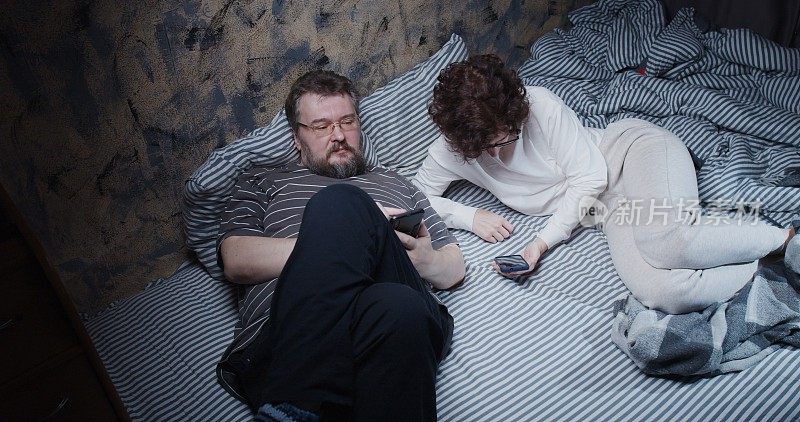 成熟的夫妻躺在床上，每个人都在用自己的智能手机交流