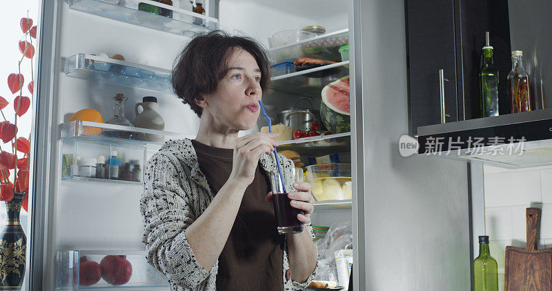 成熟的女人在冰箱旁边喝葡萄汁