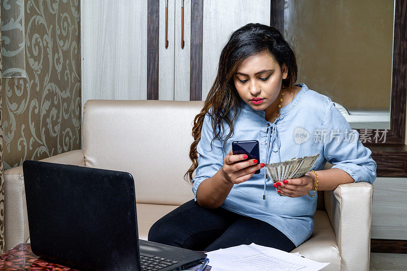 年轻女子坐在沙发上用智能手机付账单。