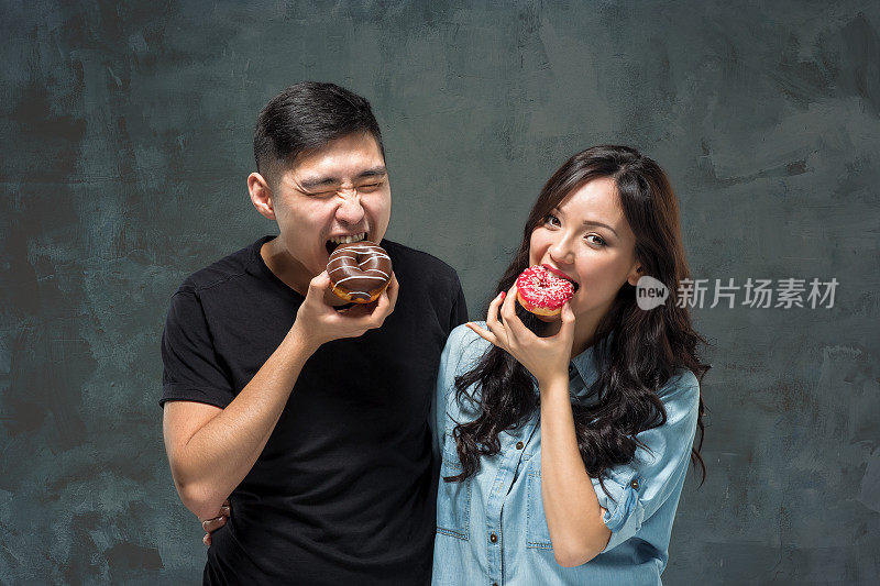 年轻的亚洲夫妇喜欢吃甜的彩色甜甜圈
