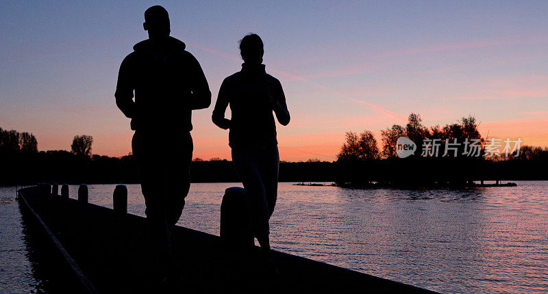 一对夫妇在黎明时分在湖上跑步的剪影