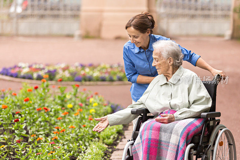 年长的妇女坐在轮椅上，由护工照顾