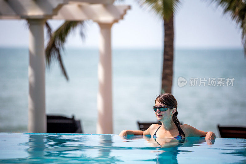 在热带度假村无限泳池内放松的女人