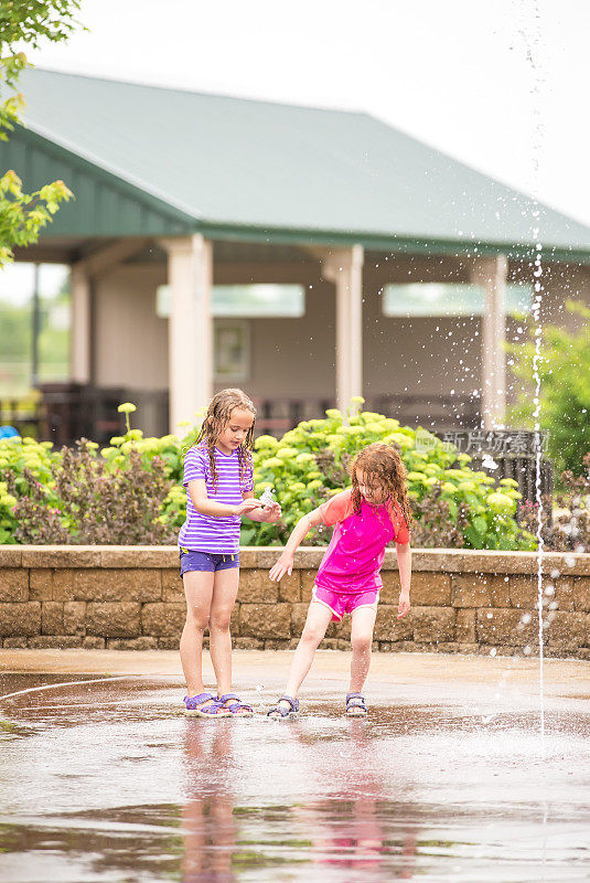 两个女孩在水花公园的喷泉里玩耍