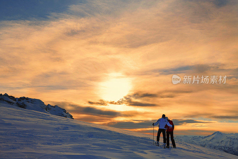 滑雪者夫妇欣赏美丽的冬季山脉日落景观