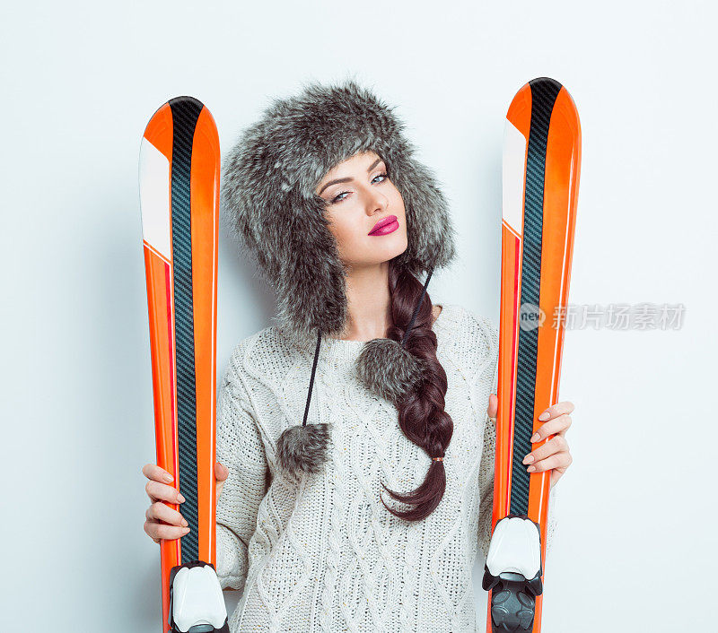 快乐的女人戴着皮帽捧着滑雪板