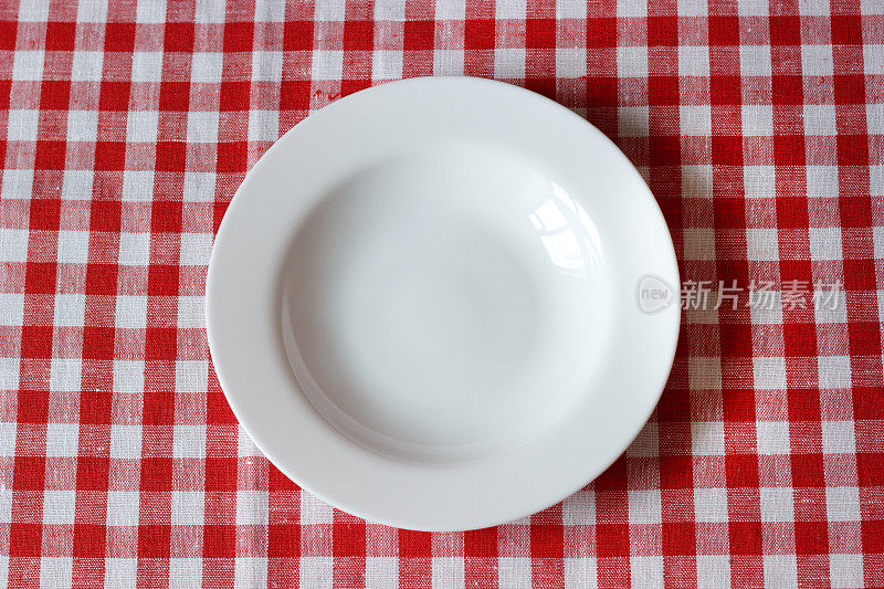 一个空盘子放在红白相间的桌布上