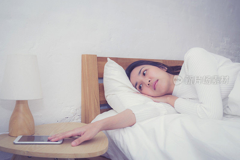 睡眼惺忪的女人在卧室里用手机闹铃醒来。