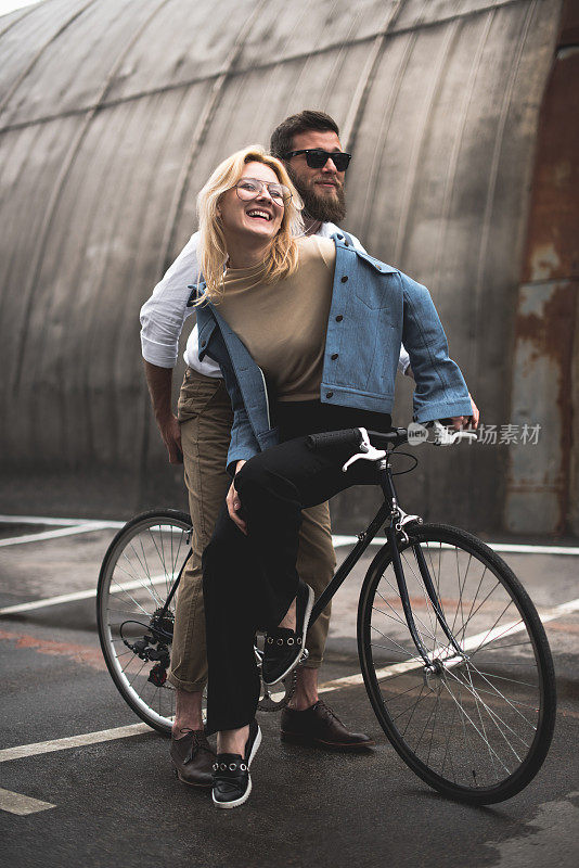 时髦开朗的年轻夫妇在停车场骑自行车