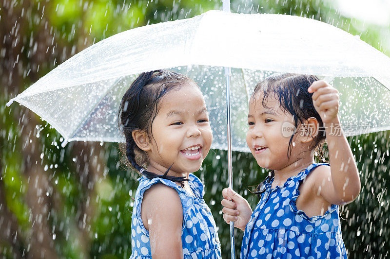 两个快乐的亚洲小女孩带着伞一起玩雨