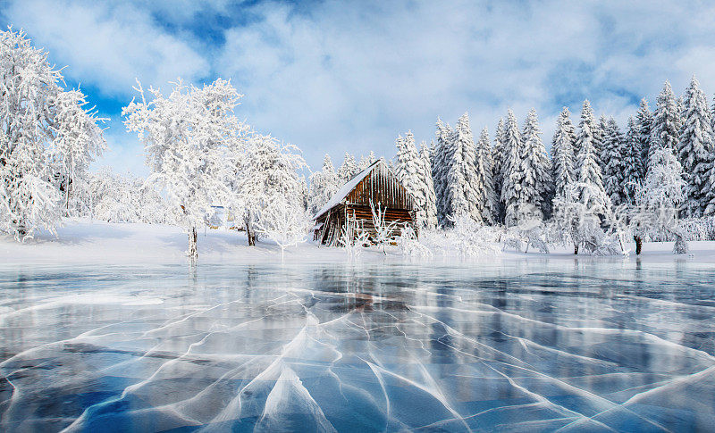 蓝色的冰和冰表面的裂缝。冬天蓝天下的冰湖。山里的小屋。神秘的雾。喀尔巴阡山。乌克兰,欧洲