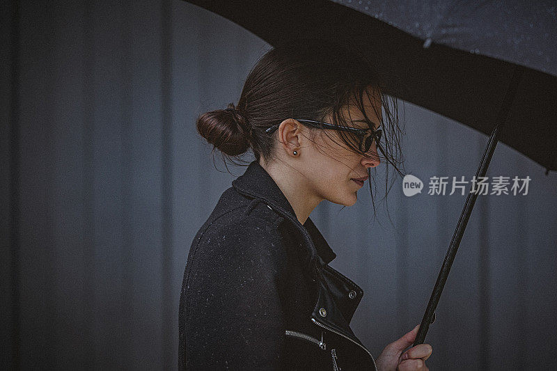 一名年轻女子撑着伞，在寒冷的秋日里在风雨中行走。