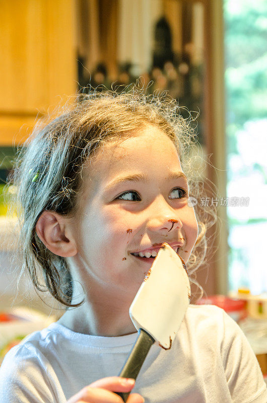 小女孩正在用锅铲吃巧克力蛋糕粉