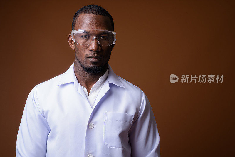 工作室拍摄的肌肉英俊的非洲男子医生戴着保护眼镜，以彩色背景