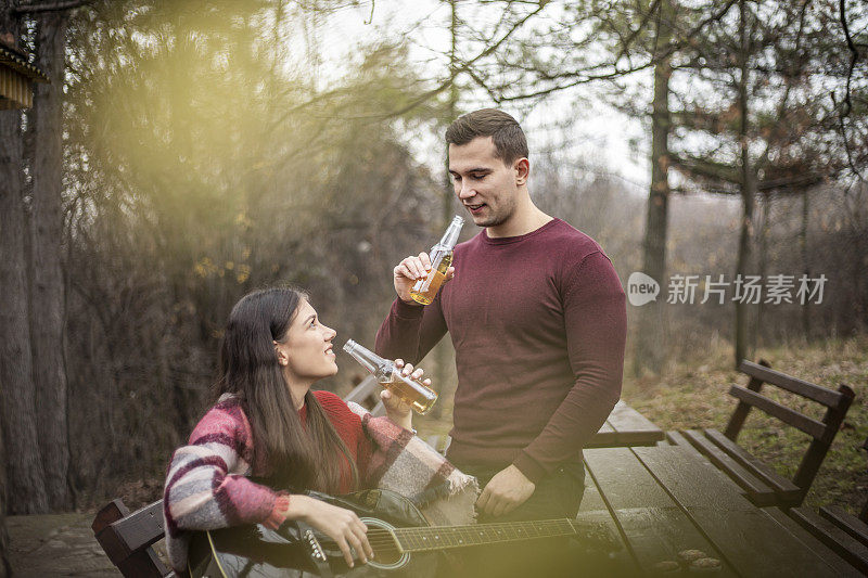 一对相爱的年轻夫妇弹吉他，花时间在大自然中，庆祝情人节——一个年轻美丽的女人愉快地坐在男孩旁边，弹他的吉他