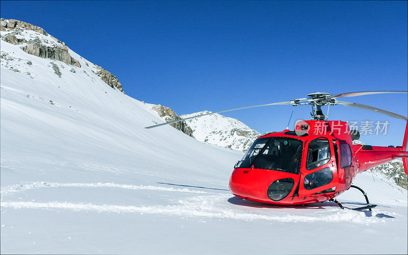 一架红色的商用直升机降落在高山的雪地上