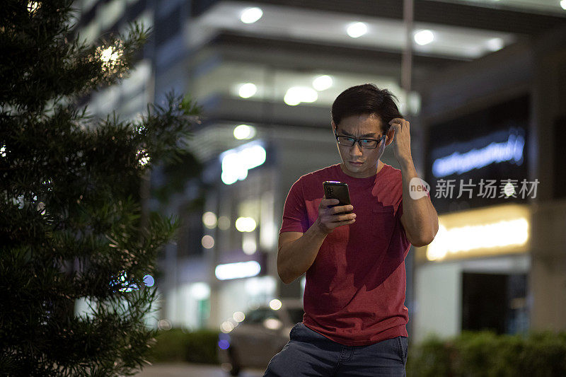 一名亚洲华人男子看着智能手机，脸上带着担忧的表情。
