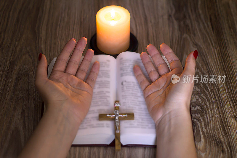 祈祷。女人的手靠近圣经和木桌上的蜡烛。
