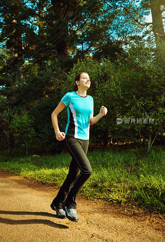 年轻的女性跑步者在一个美丽的阳光灿烂的森林里锻炼