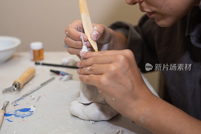 工匠的手用粘土和模塑糊在桌子上用几个模塑工具和刷子塑造一个雕塑