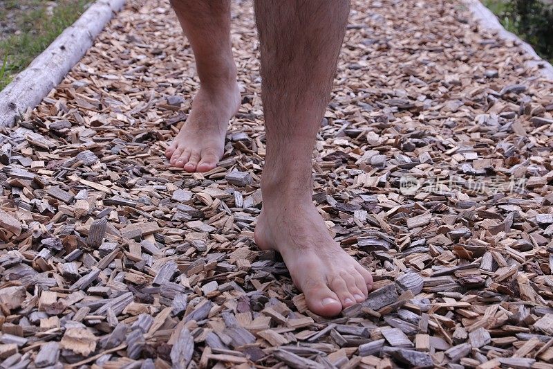 一个人光着脚走在有木屑的小路上