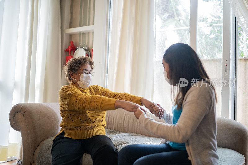 物理治疗师帮助老年妇女在家做运动-使用防护口罩