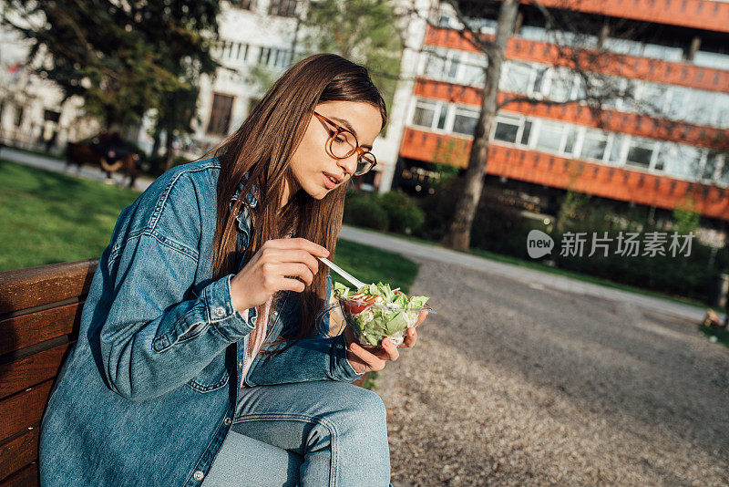 一个美丽的女孩在公园里吃着健康的沙拉