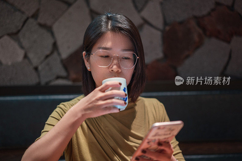 一位美丽的亚洲女子一边喝茶一边用手机