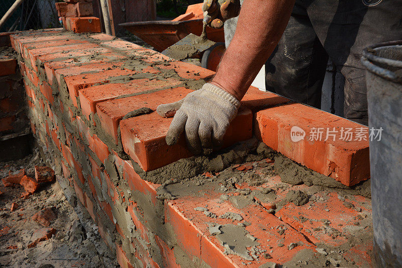 砌筑施工。一个泥瓦匠，一个泥瓦匠正在铺设，安装砖，使用灰泥和泥铲，为新房子砌砖墙。