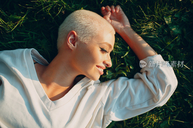 千禧年年轻女子金发短发户外微笑躺在草地上的肖像。