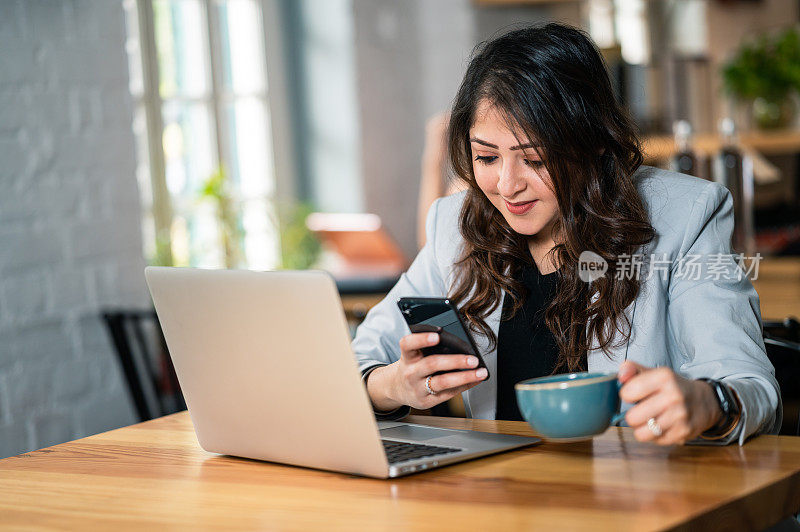 在咖啡馆工作的女性，一边使用笔记本电脑，一边用智能手机发短信