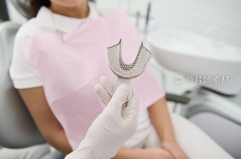 一个牙医的手握牙科模具牙医的牙齿陶瓷板铸造的背景病人坐在牙医的椅子在牙科诊所